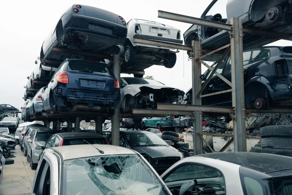 Is It Better to Book Directly With a Carrier or a Broker? Stacked salvage vehicles in scrapyard, highlighting carrier handling differences in broker vs carrier auto transport.