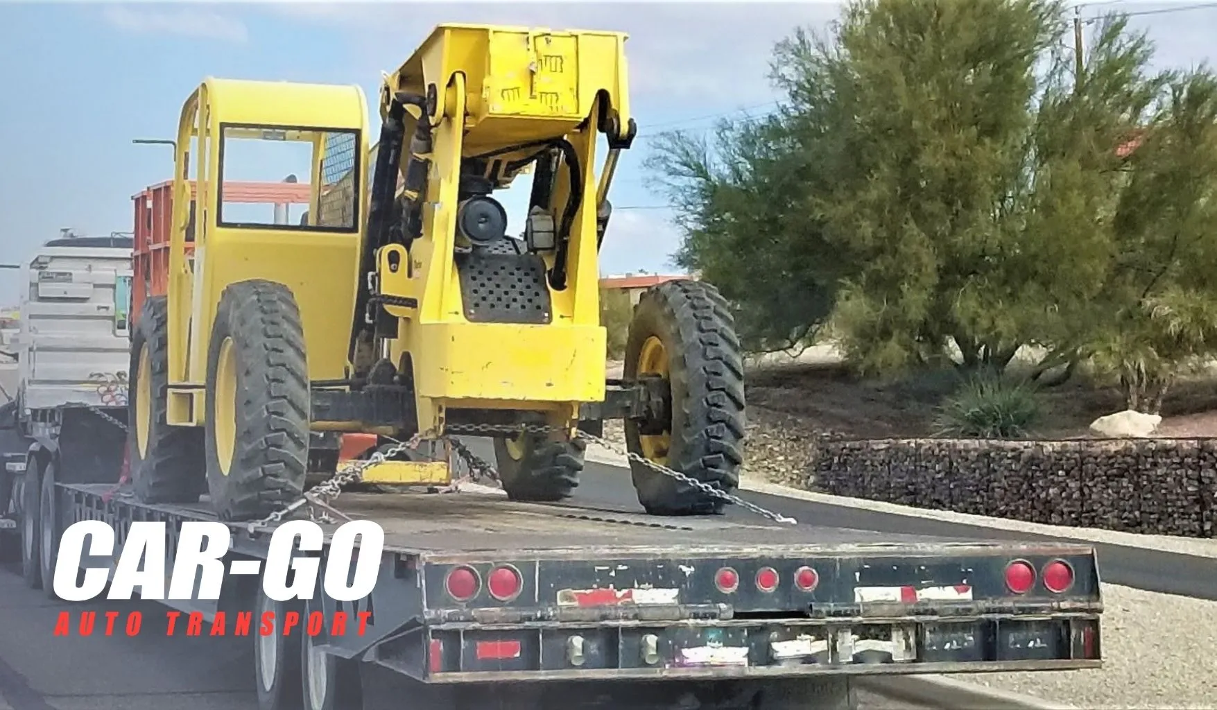 Shipping oversized vehicles with yellow construction equipment chained to a flatbed trailer