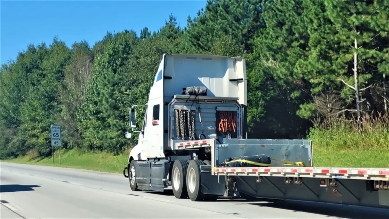 Shipping oversized vehicles with a white semi pulling a flatbed trailer on a rural highway